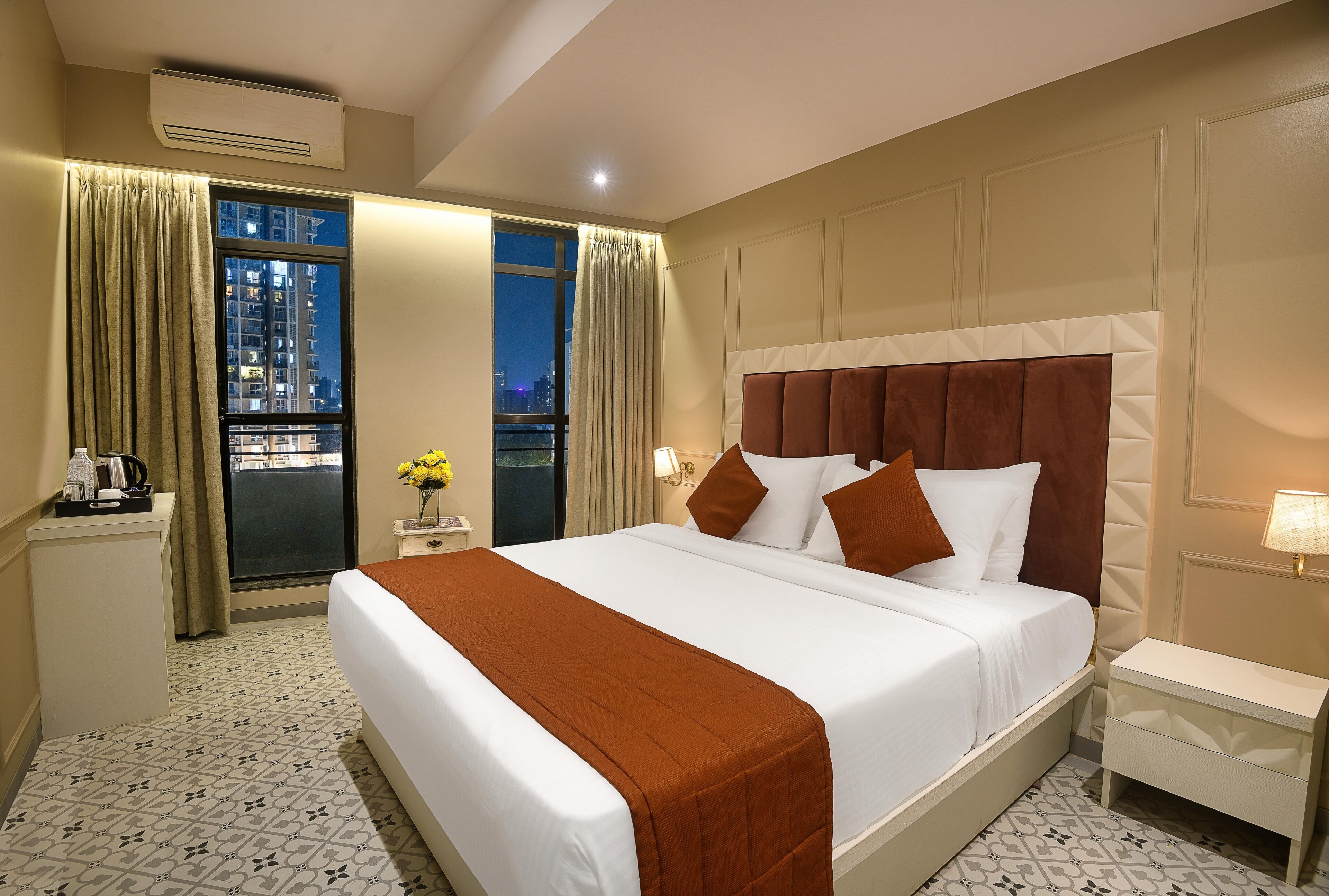 Een hotelkamer met een groot bed, een nachtkastje, een bureau met lamp en uitzicht op de stad 's nachts.