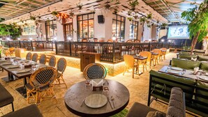 Un restaurant intérieur avec des tables rondes, des chaises en osier et des plantes suspendues.