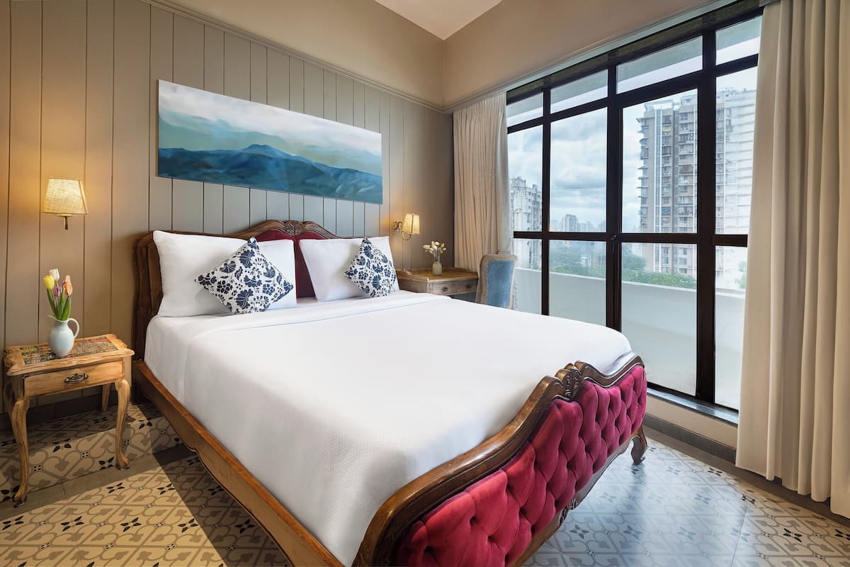 Quarto de hotel com uma cama grande, vista para edifícios pela janela e um quadro na parede.