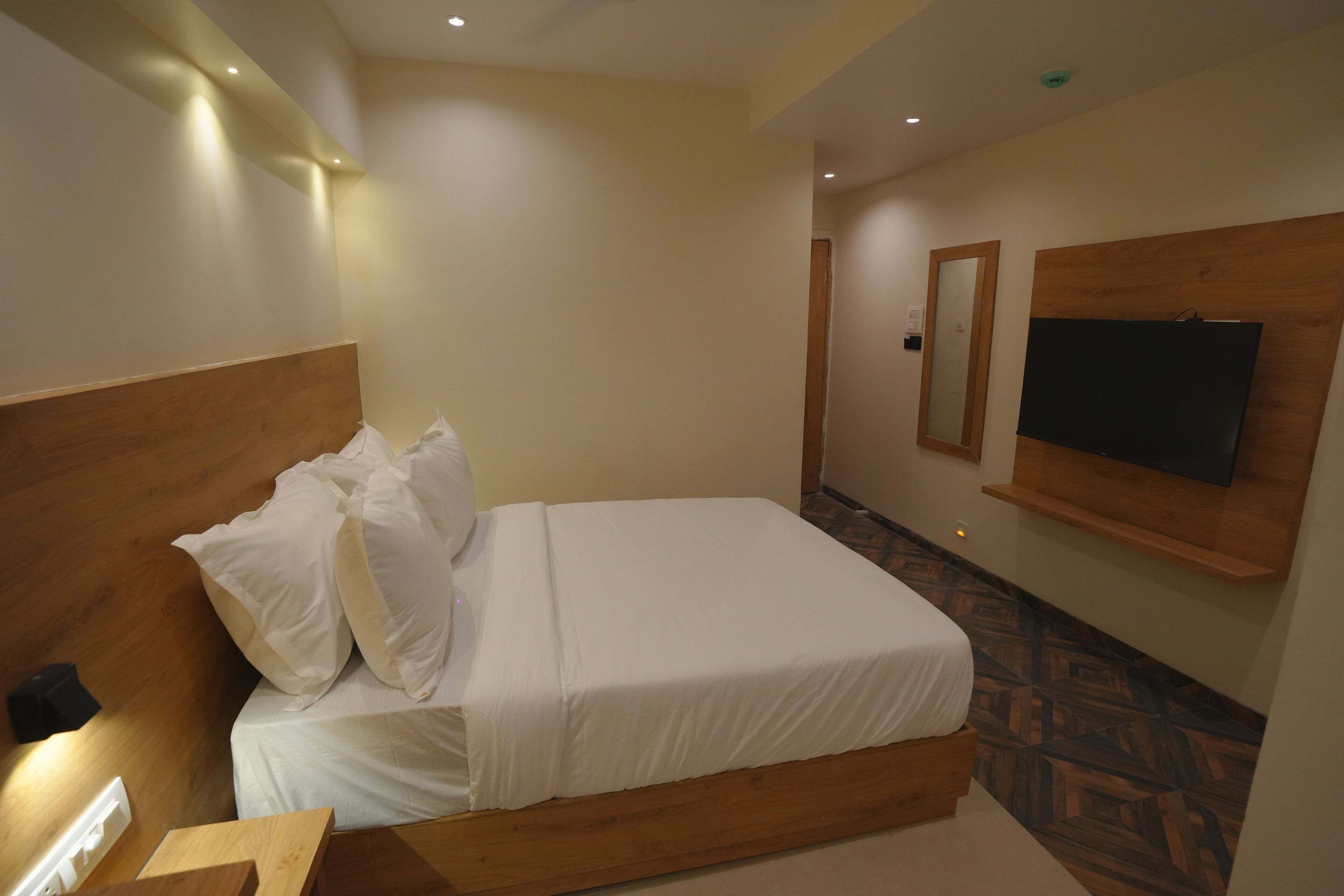 Une chambre d ’hôtel avec une tête de lit en bois, un lit recouvert de draps blancs, un téléviseur fixé au mur et un sol à motifs.