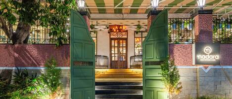 A hotel entrance with a green gate, steps leading up to a door, and potted plants.