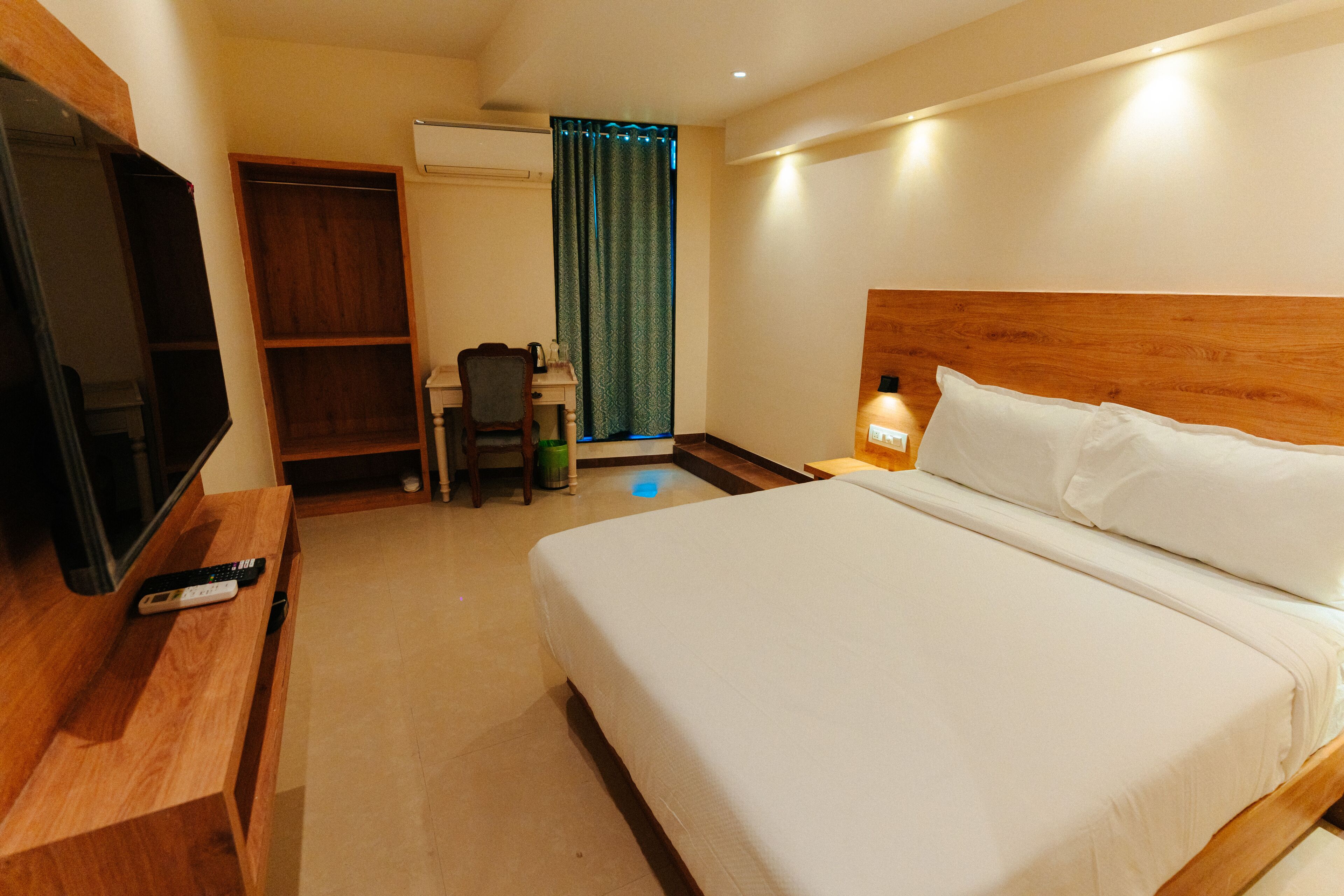 A hotel room with a bed, a TV on a wooden stand, a desk with a chair, and a wardrobe.