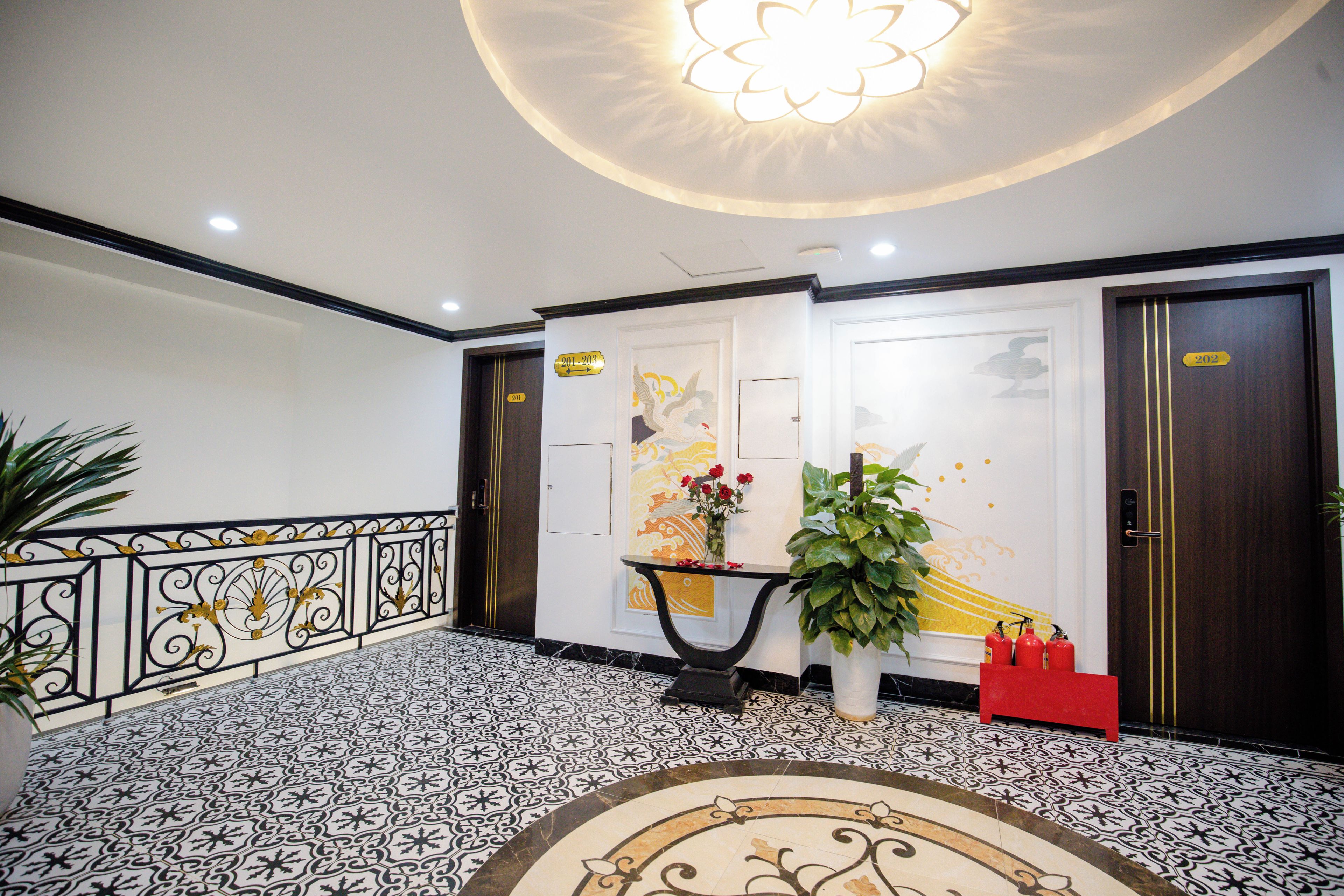 Un hall de hotel con piso estampado, un mostrador de recepción, una planta en maceta y extintores.