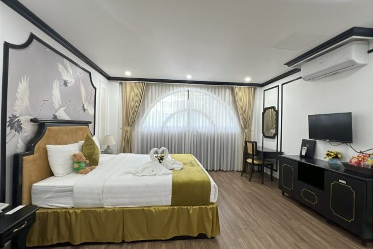 A hotel room with a bed, a television, a desk, and a large window with curtains.