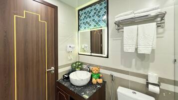 A bathroom with a wooden door, a marble sink, a mirror, a towel rack, and a teddy bear on the counter.
