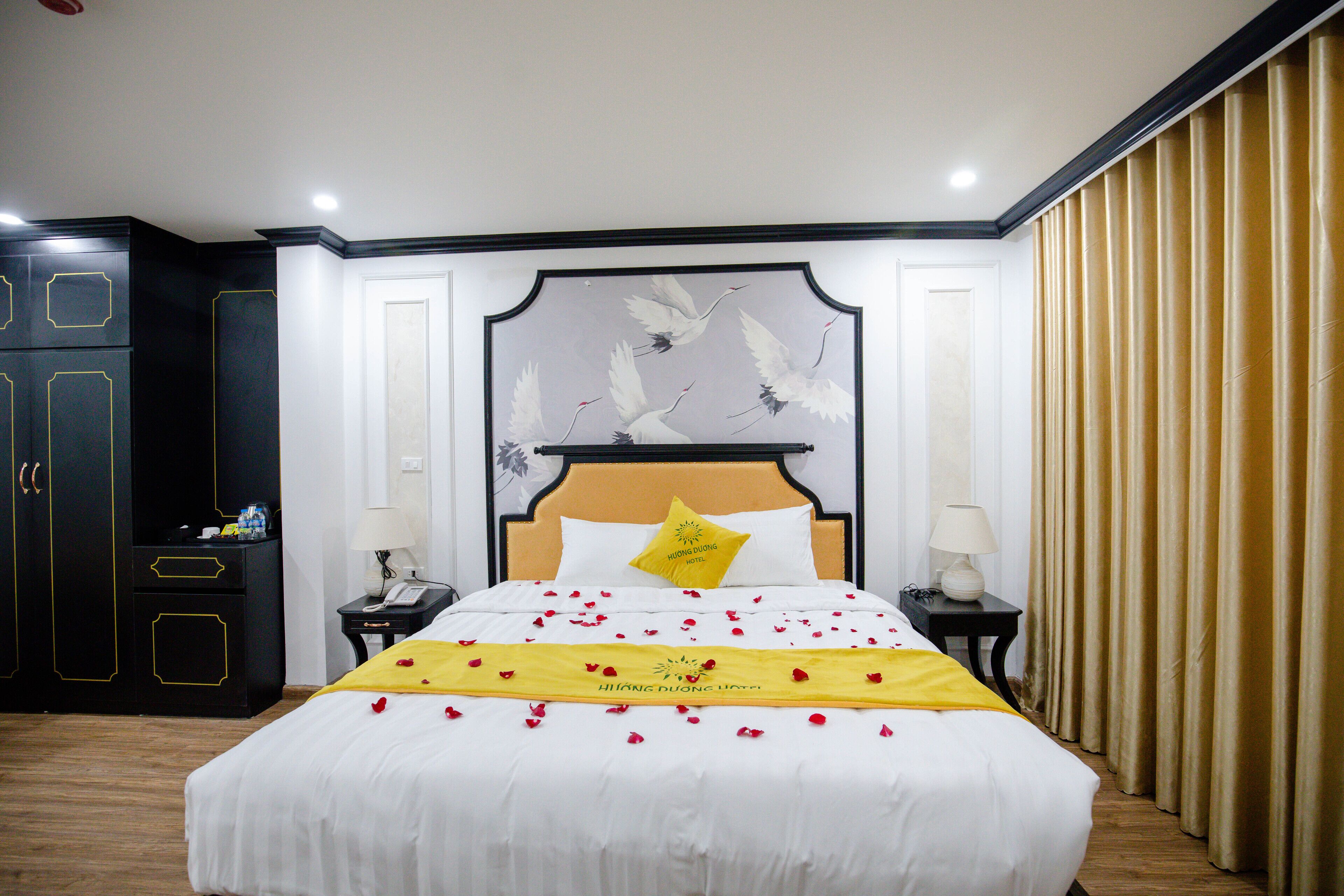 Un lit bien fait, recouvert d’une couvre-lit blanche et agrémenté d’un objet décoratif jaune, une table de chevet avec une lampe et une armoire à la finition noire.