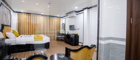 Habitación de hotel con cama, escritorio, silla y una pared divisoria de vidrio.