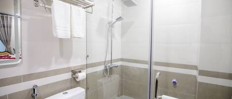 A bathroom with a glass-enclosed shower, a toilet, and a towel rack with folded towels.