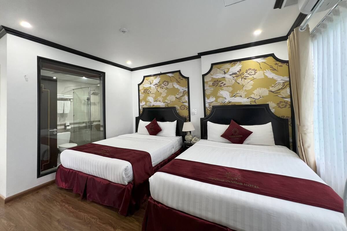 Quarto de hotel com duas camas, box de vidro para o chuveiro e papel de parede floral.