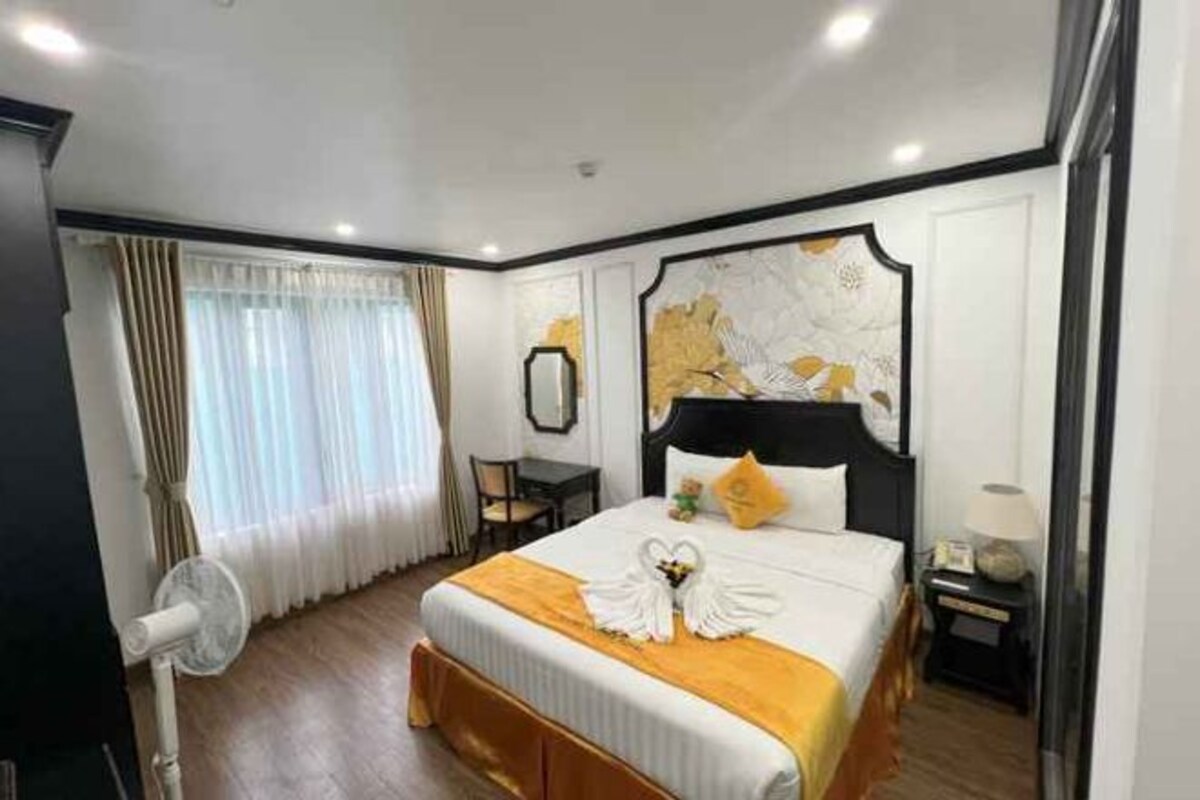 A hotel room with a large bed, a desk, a chair, and a fan.
