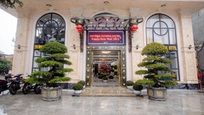 The entrance of Huong Duong Hotel with a traditional architectural style, featuring a central doorway flanked by potted topiaries and a digital signboard displaying a New Year greeting. - Huong Duong Hotel Thanh Hoa (Hac Thanh)