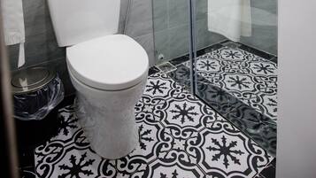 Een badkamer met toilet, een douchecabine van glas en vloertegels met een patroon.