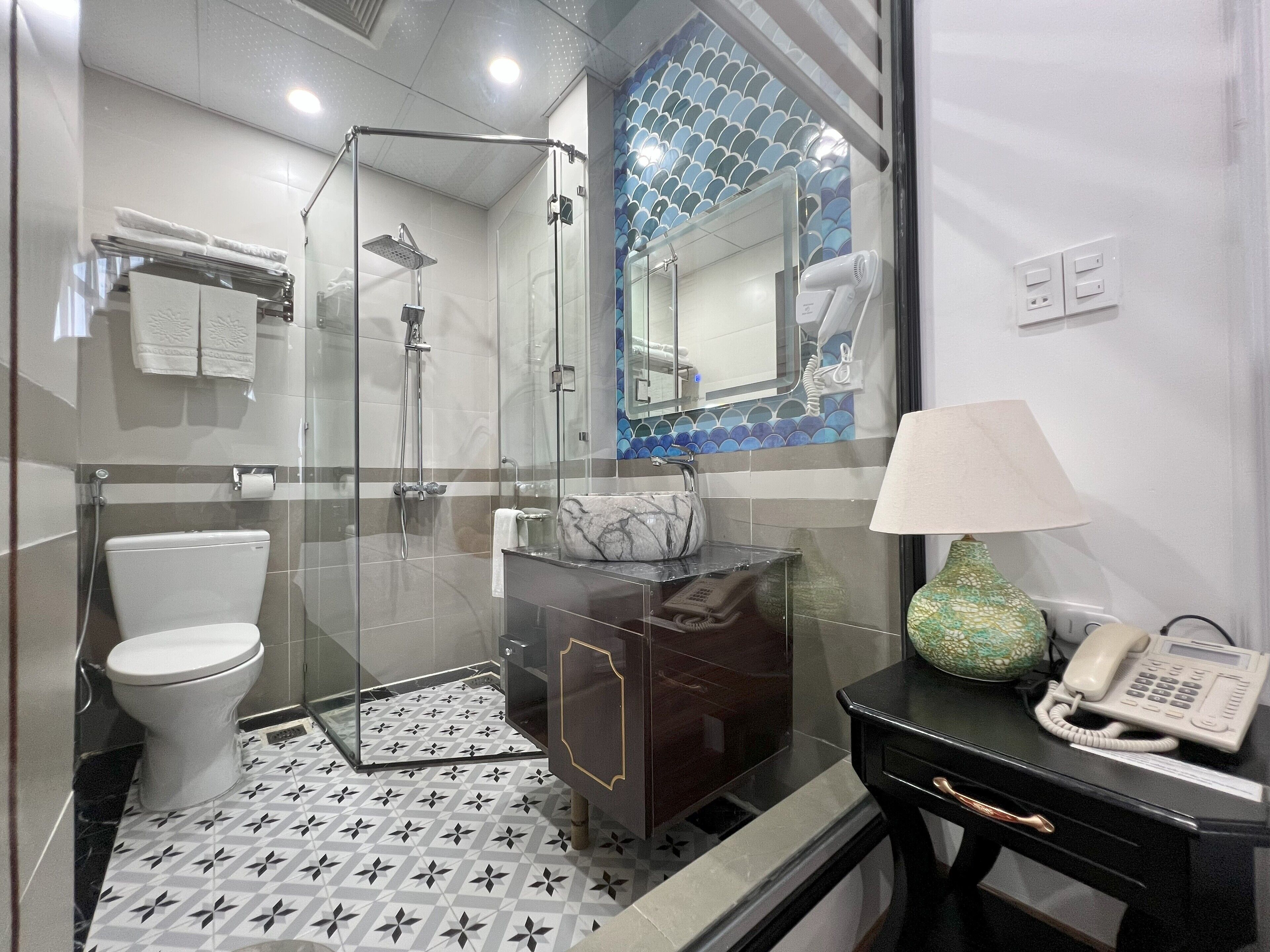 A modern bathroom with a glass-enclosed shower, a toilet, a vanity with a marble sink, and a telephone.