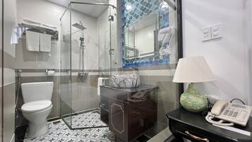 A modern bathroom with a glass-enclosed shower, a toilet, a vanity with a marble sink, and a telephone.