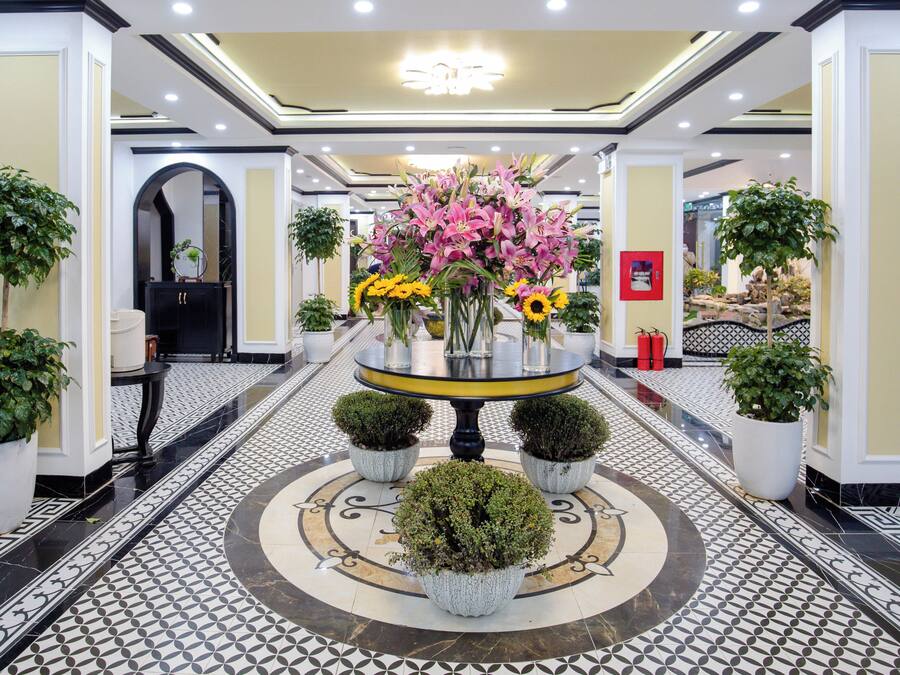Un vestíbulo de hotel con una mesa redonda central rodeada de plantas y flores en macetas.