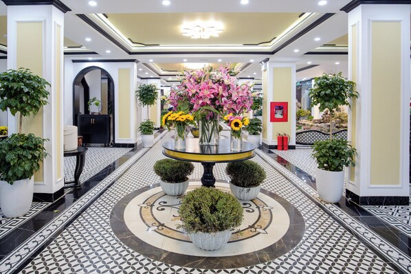 Un vestíbulo de hotel con una mesa redonda central rodeada de plantas y flores en macetas.