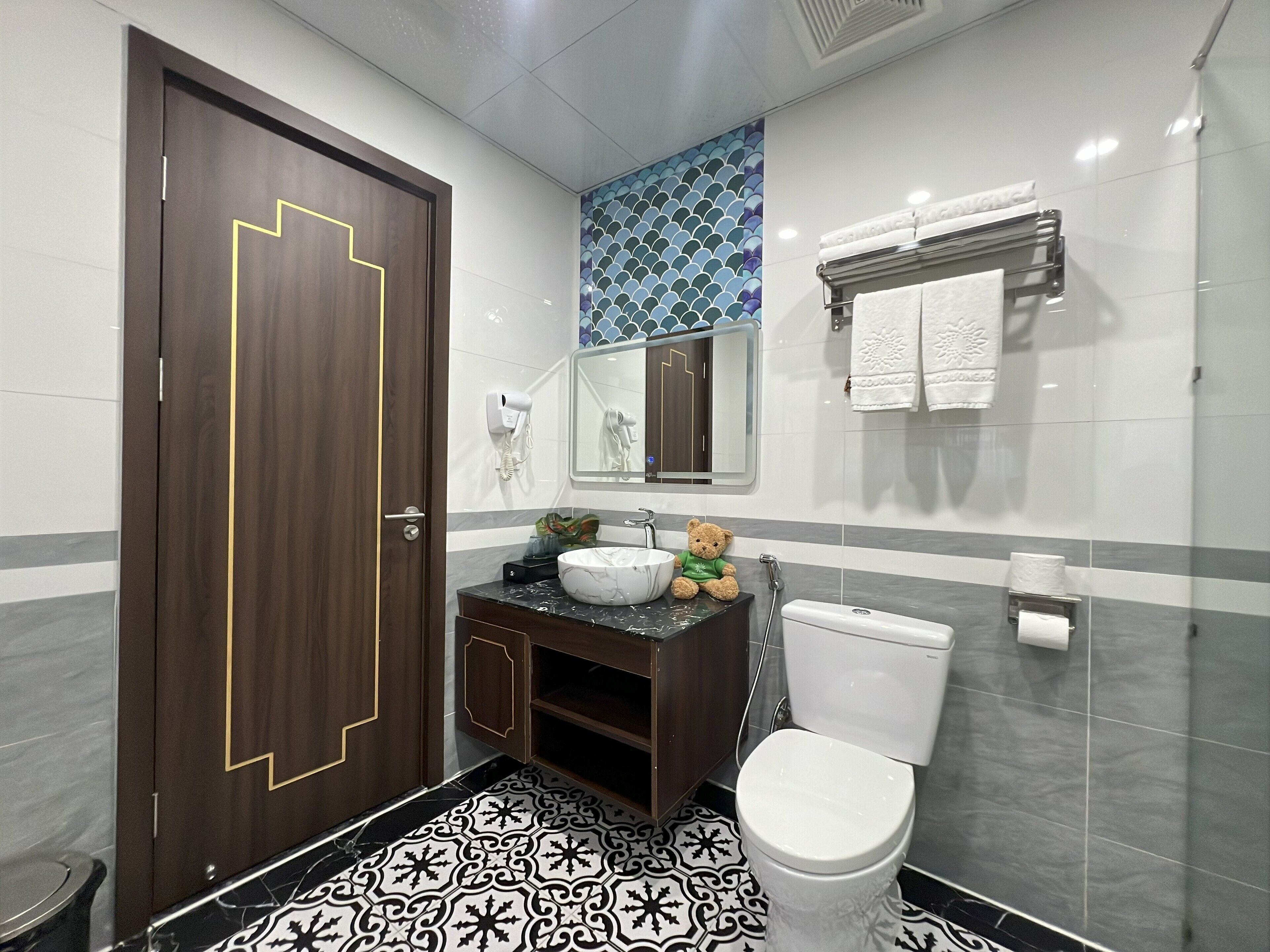 Une salle de bain moderne avec une porte en bois foncé, des toilettes blanches, un lavabo en marbre et un porte-serviettes.