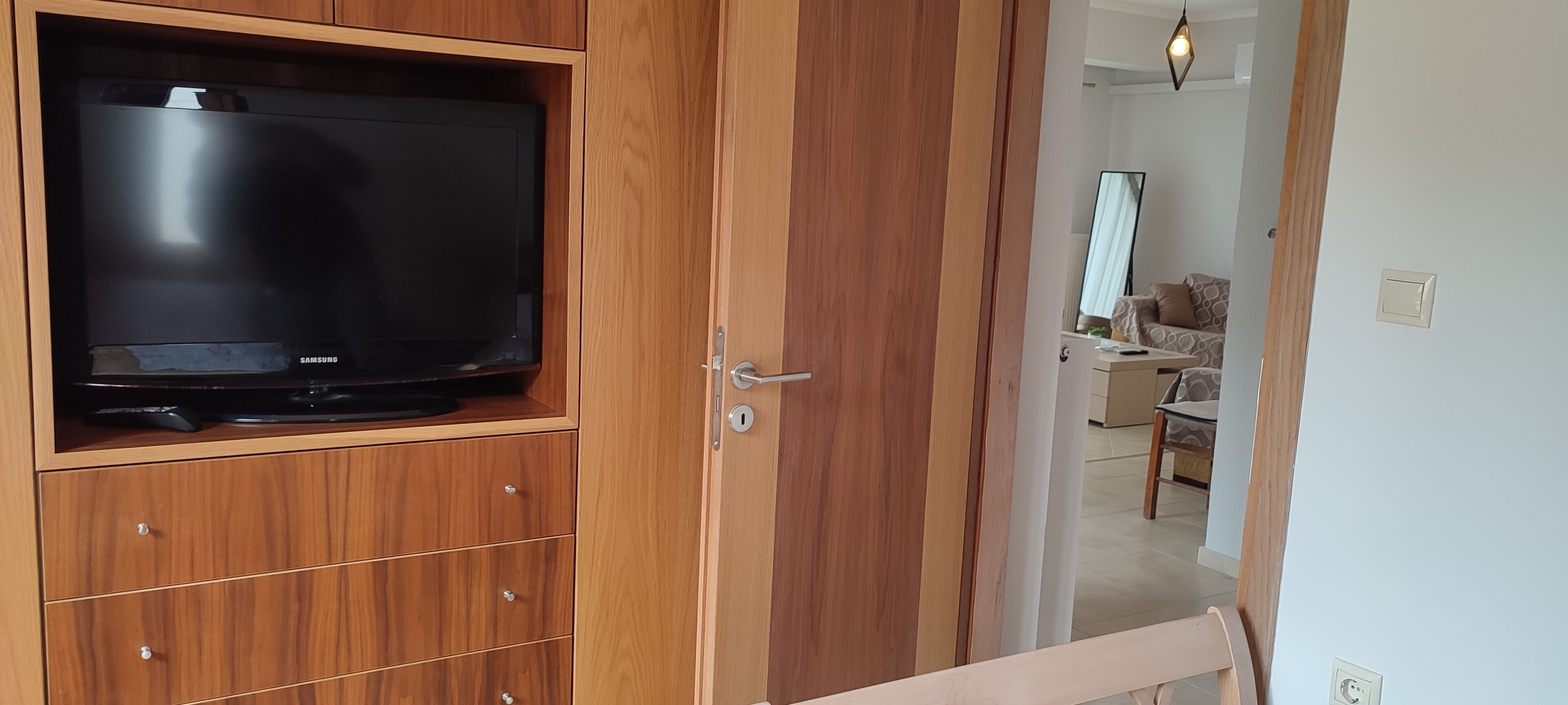 Ein Holzkabinett mit einem Fernseher, einer Tür mit Schloss und einem Blick in ein Wohnzimmer mit Sofa und Lampe.