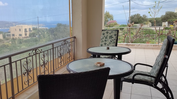 A balcony with a view of a coastal area, featuring a round table and two wicker chairs.