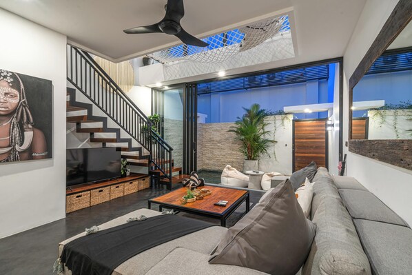A modern living room with a staircase, a flat-screen TV, a coffee table, and a sofa.