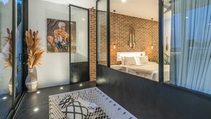 A modern interior with a brick wall, a bed with white bedding, and a painting on the wall. - Loft Erika (Canggu)