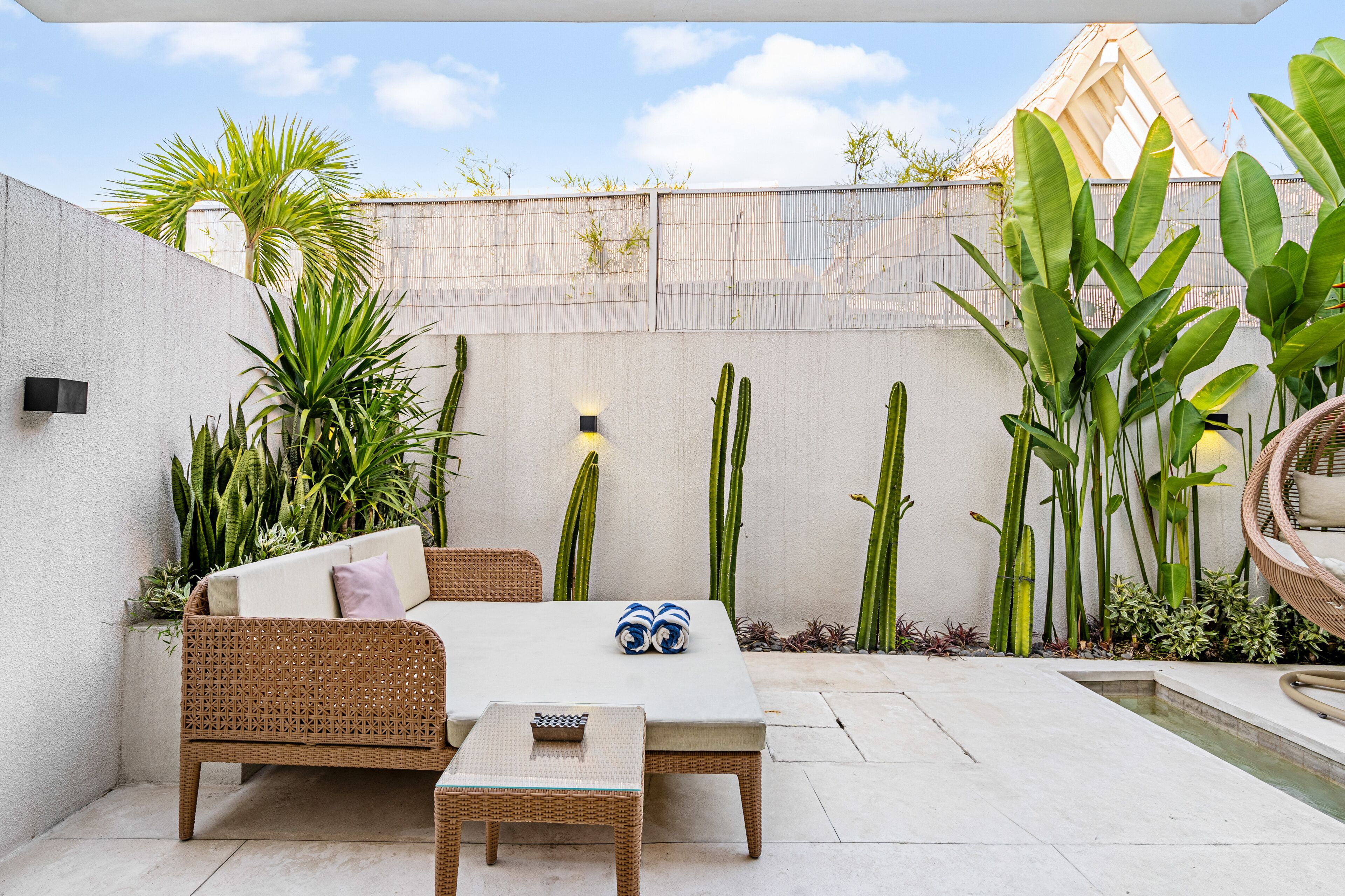 Un patio con un sofá de mimbre, una mesita y una piscina.