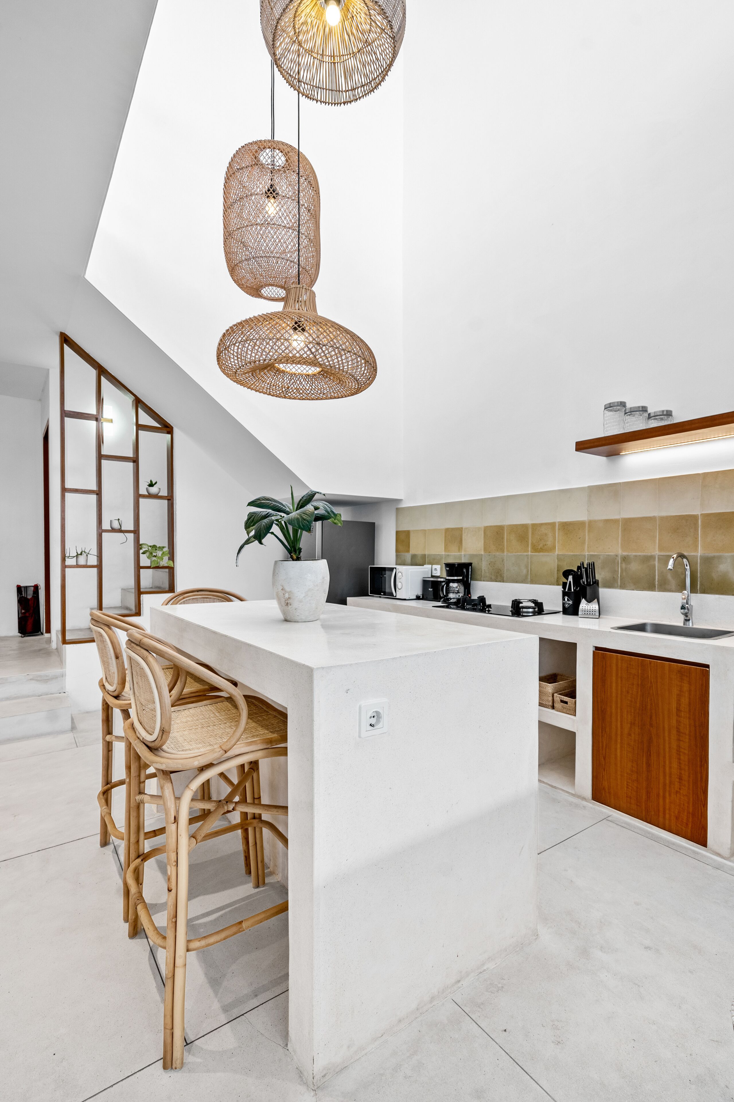 A modern kitchen with a central island, wicker pendant lights, and a dining area with rattan chairs.