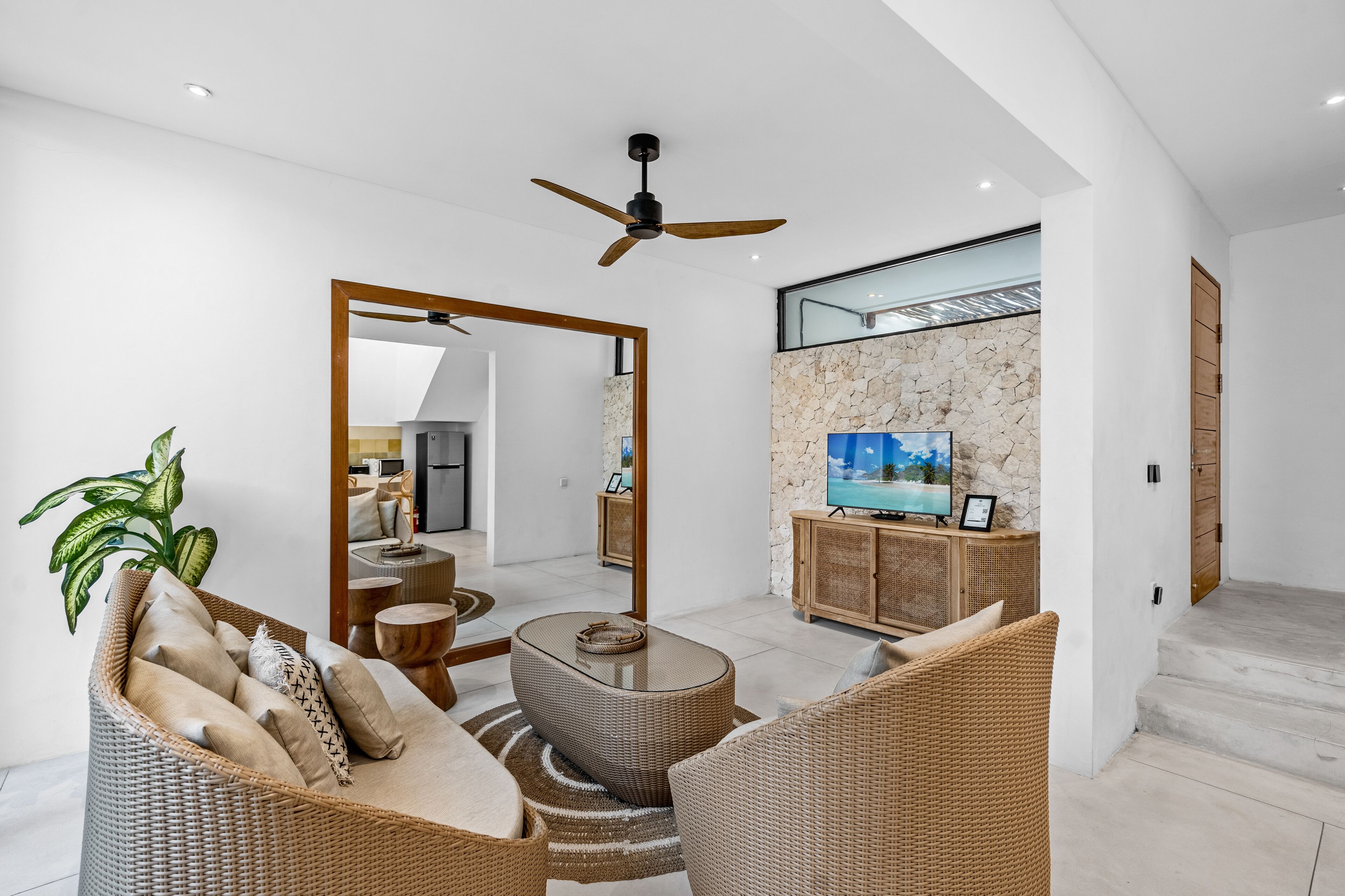 A modern living room with wicker furniture, a ceiling fan, a stone wall, and a television.
