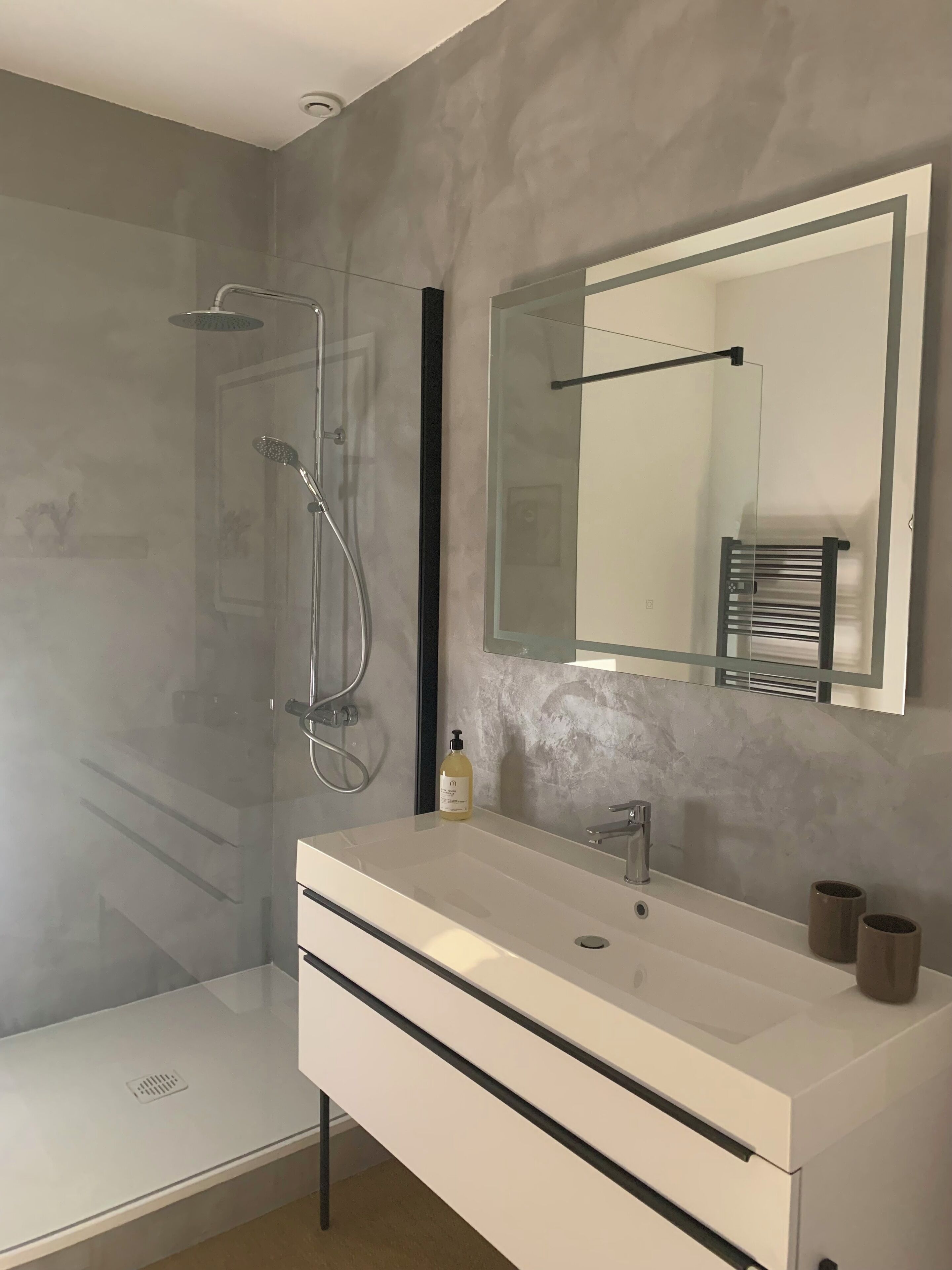 Une salle de bain moderne avec une douche à parois de verre, un grand miroir et un meuble-lavabo blanc.