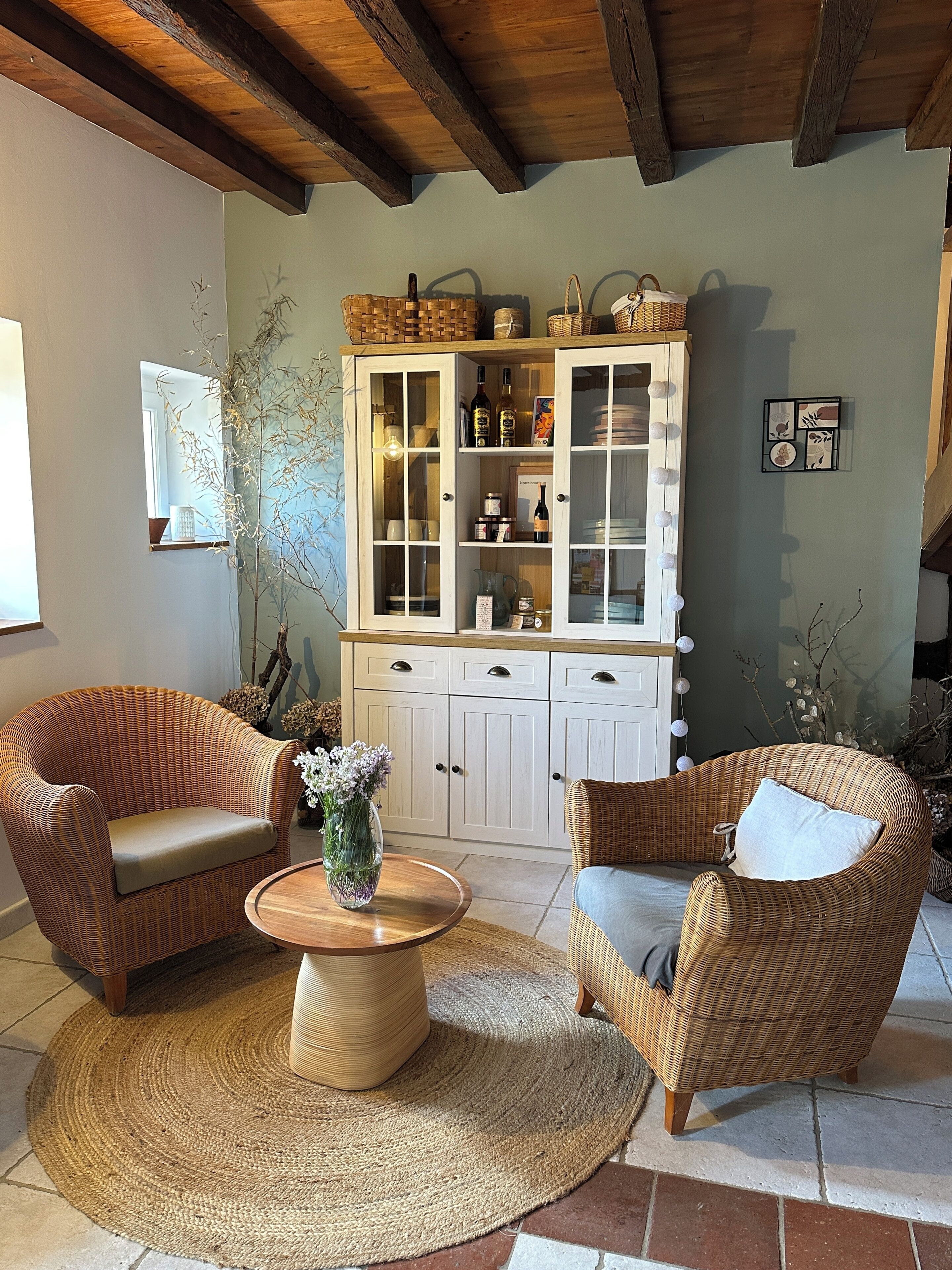 Une pièce chaleureuse, meublée de meubles en osier, avec un buffet en bois aux portes vitrées et un tapis tissé.