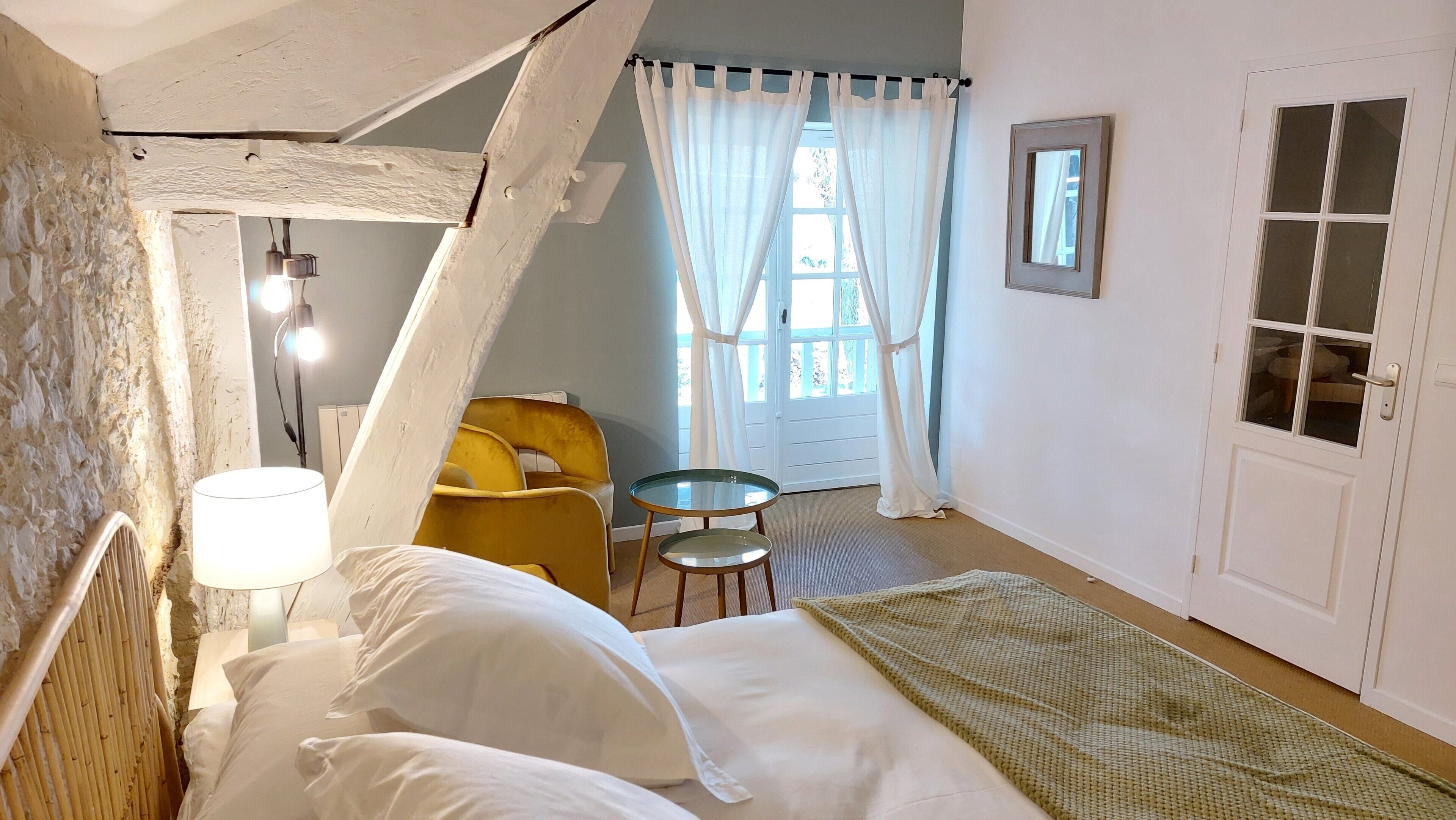 A bedroom with a bed, a chair, a small table, a lamp, and a door with a window.