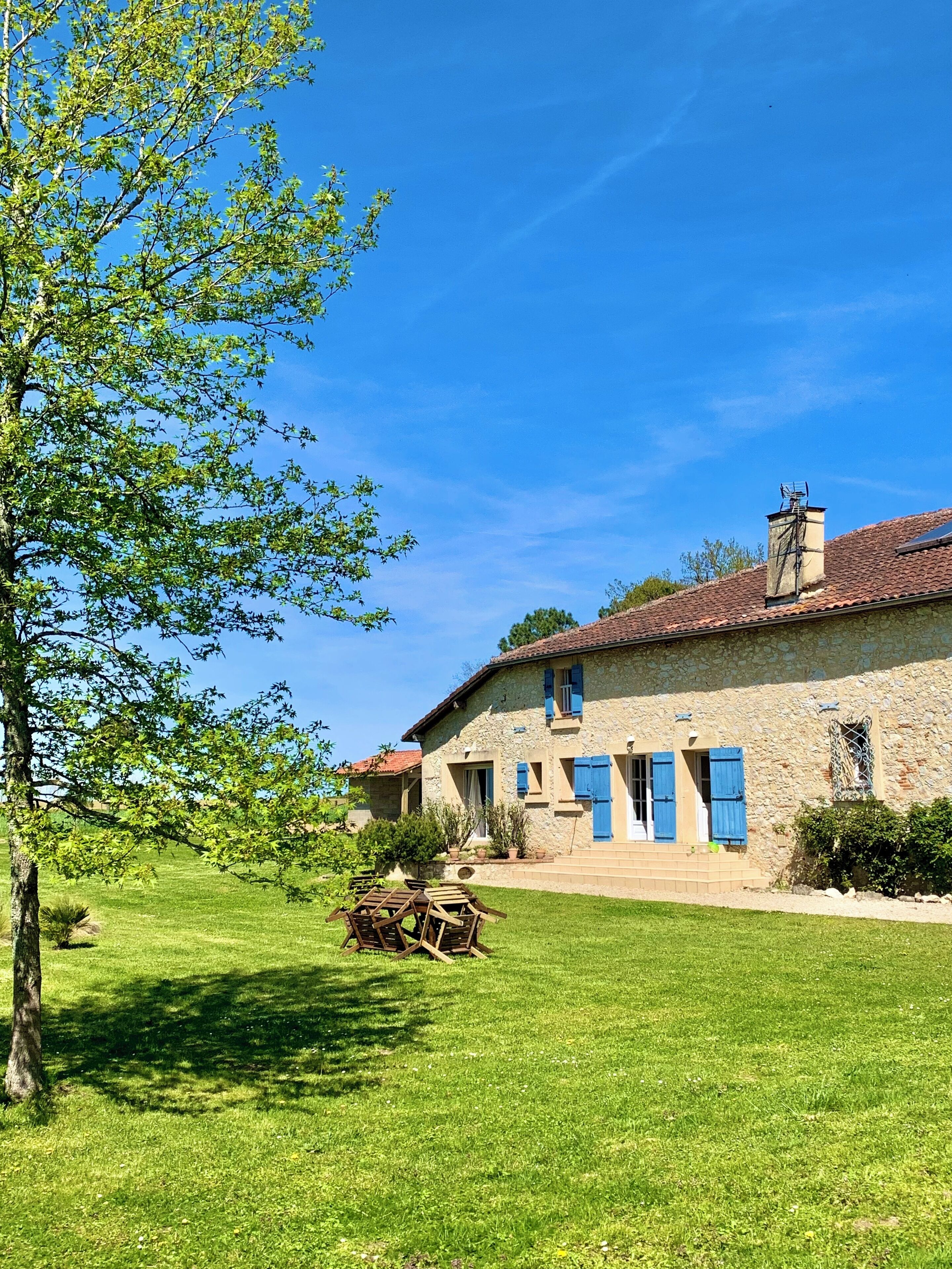 A stone house with blue shutters, a tiled roof, and a well-maintained lawn.