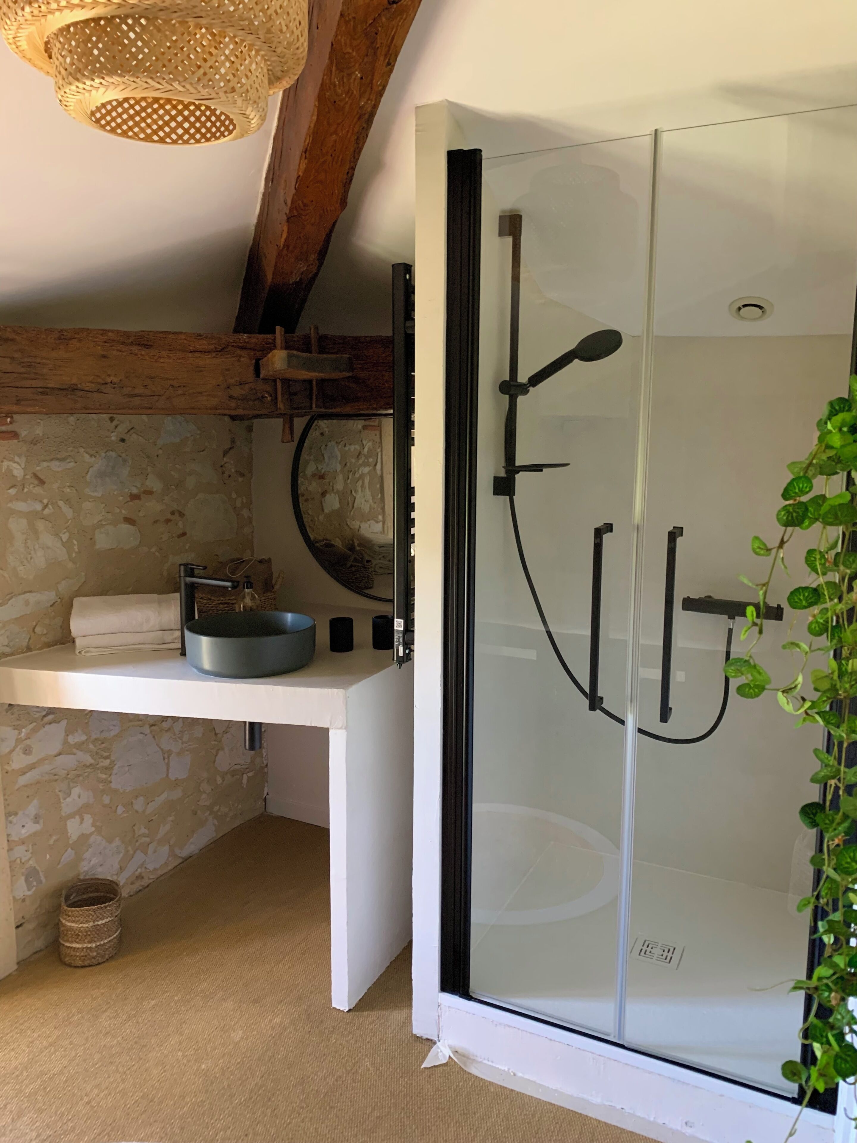 A bathroom with a glass shower enclosure, a white sink with a round basin, and a woven light fixture.