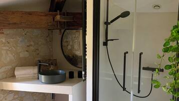 A bathroom with a glass shower enclosure, a white sink with a round basin, and a woven light fixture.
