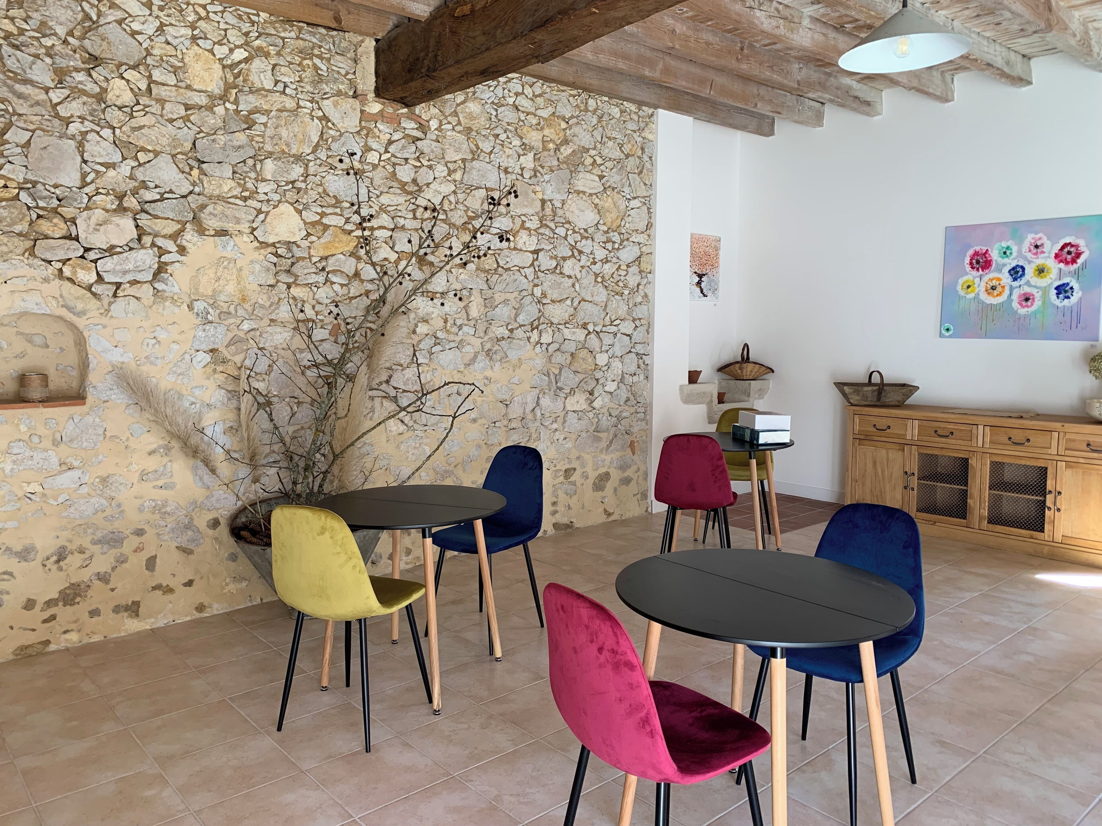 Ein rustikales Interieur mit Steinwänden, Holzbalken und einem Essbereich mit bunten Stühlen sowie einem Holzschrank.