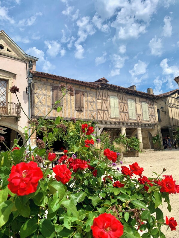 A traditional half-timbered building with a courtyard and red flowers in the foreground. - Le Poutic (Créon-d'Armagnac)