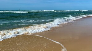 Una playa con olas suaves lamiendo la orilla, cielo despejado y un barco a lo lejos.