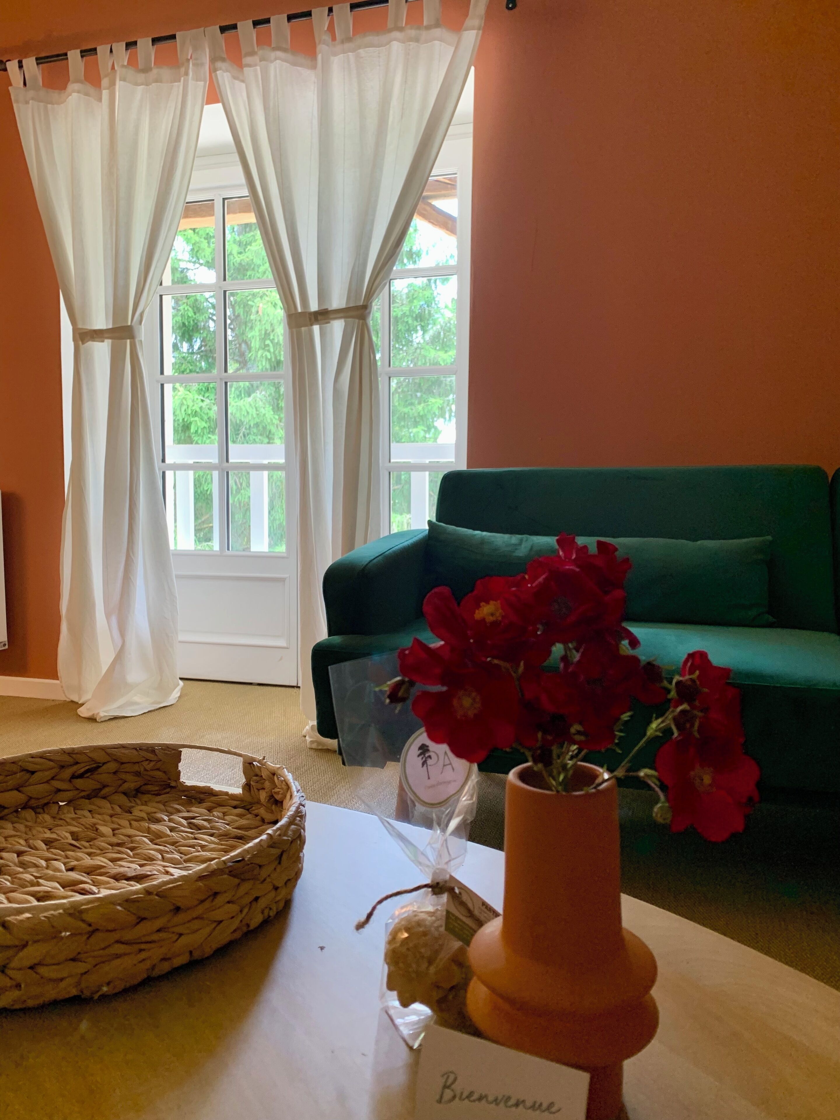 Una habitación con un sofá verde, una cesta de mimbre, un jarrón con flores rojas y un letrero de bienvenida.