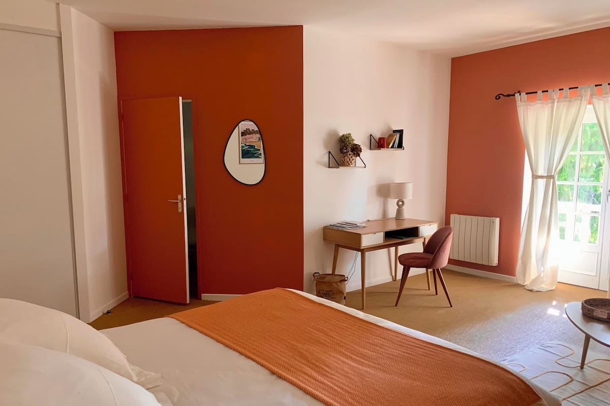 A hotel room with a bed, a desk, a chair, a radiator, and a window with curtains.