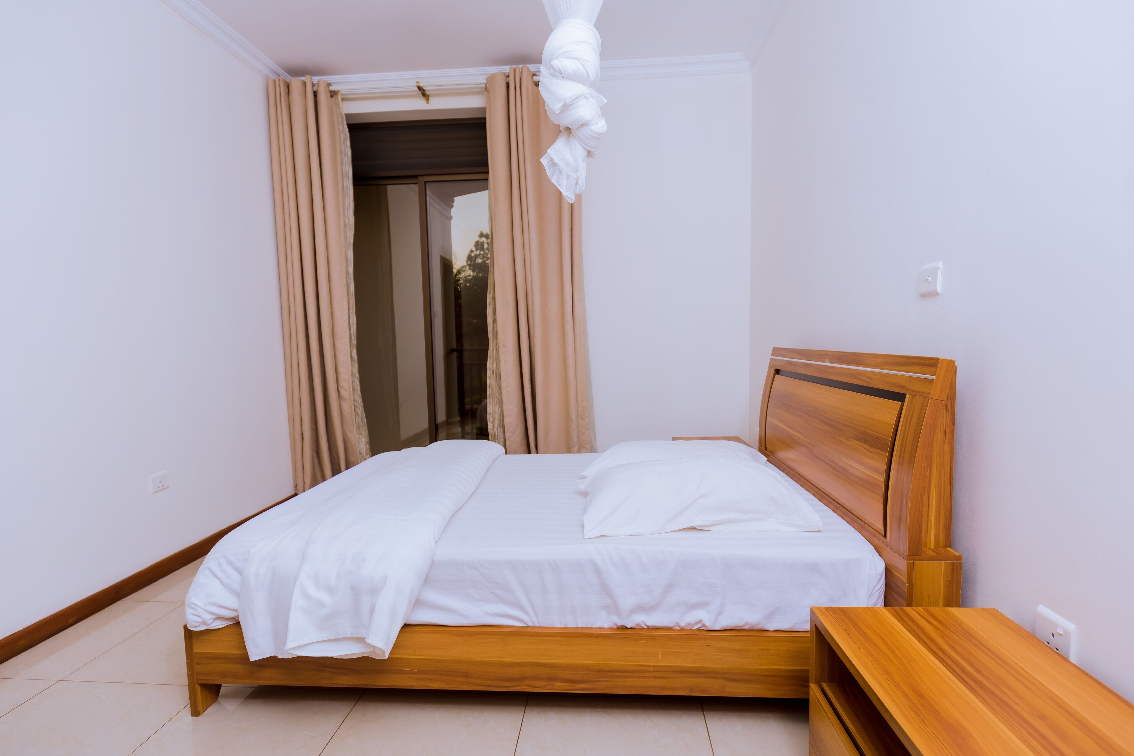 Una cama bien hecha con sábanas blancas en una habitación con cabecera y mesita de noche de madera.