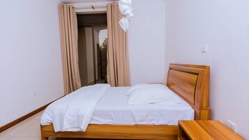 Una cama bien hecha con sábanas blancas en una habitación con cabecera y mesita de noche de madera.