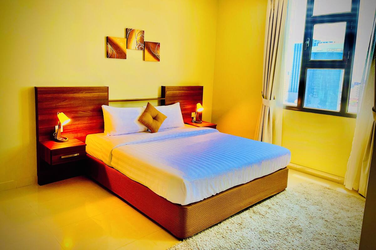 A neatly made bed with a wooden headboard, two bedside lamps, and a window with curtains.