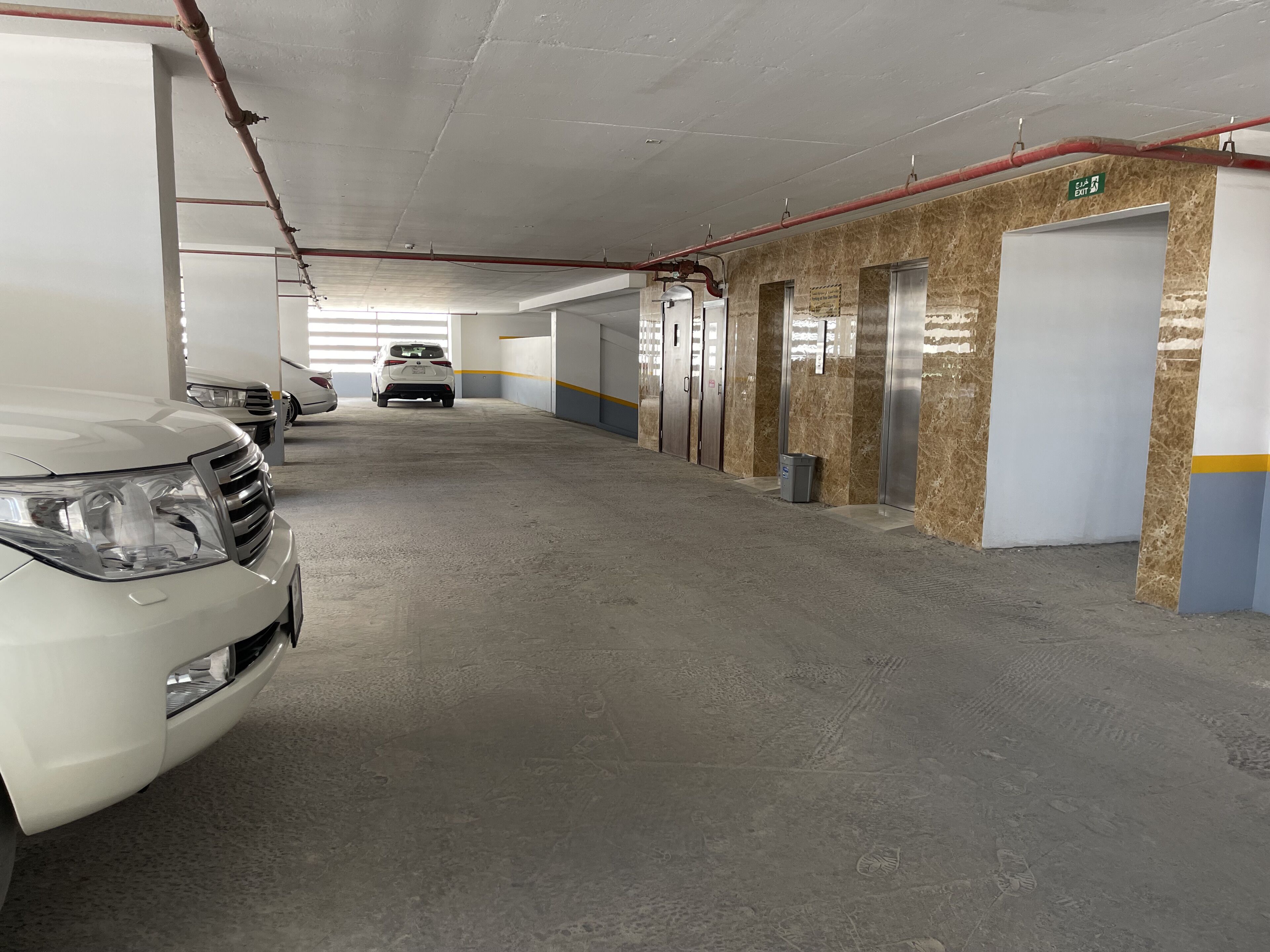 A parking garage with multiple white cars parked in rows, concrete floors, and walls with a marble-like finish.