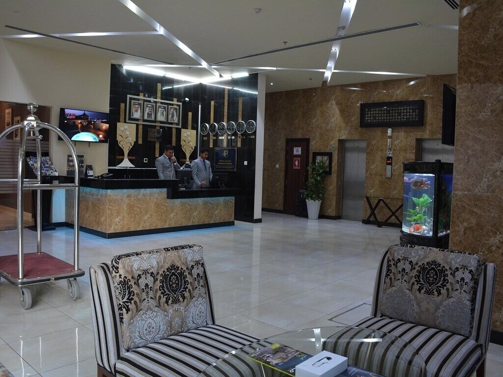 Eine Hotellobby mit einer Rezeption, zwei Sofas, einem Aquarium und einer großen Wanduhr.