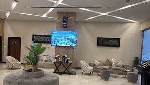 A modern hotel lobby with a large flat-screen TV, comfortable seating, and a decorative plant. - HAVEN TOWER (Manama)