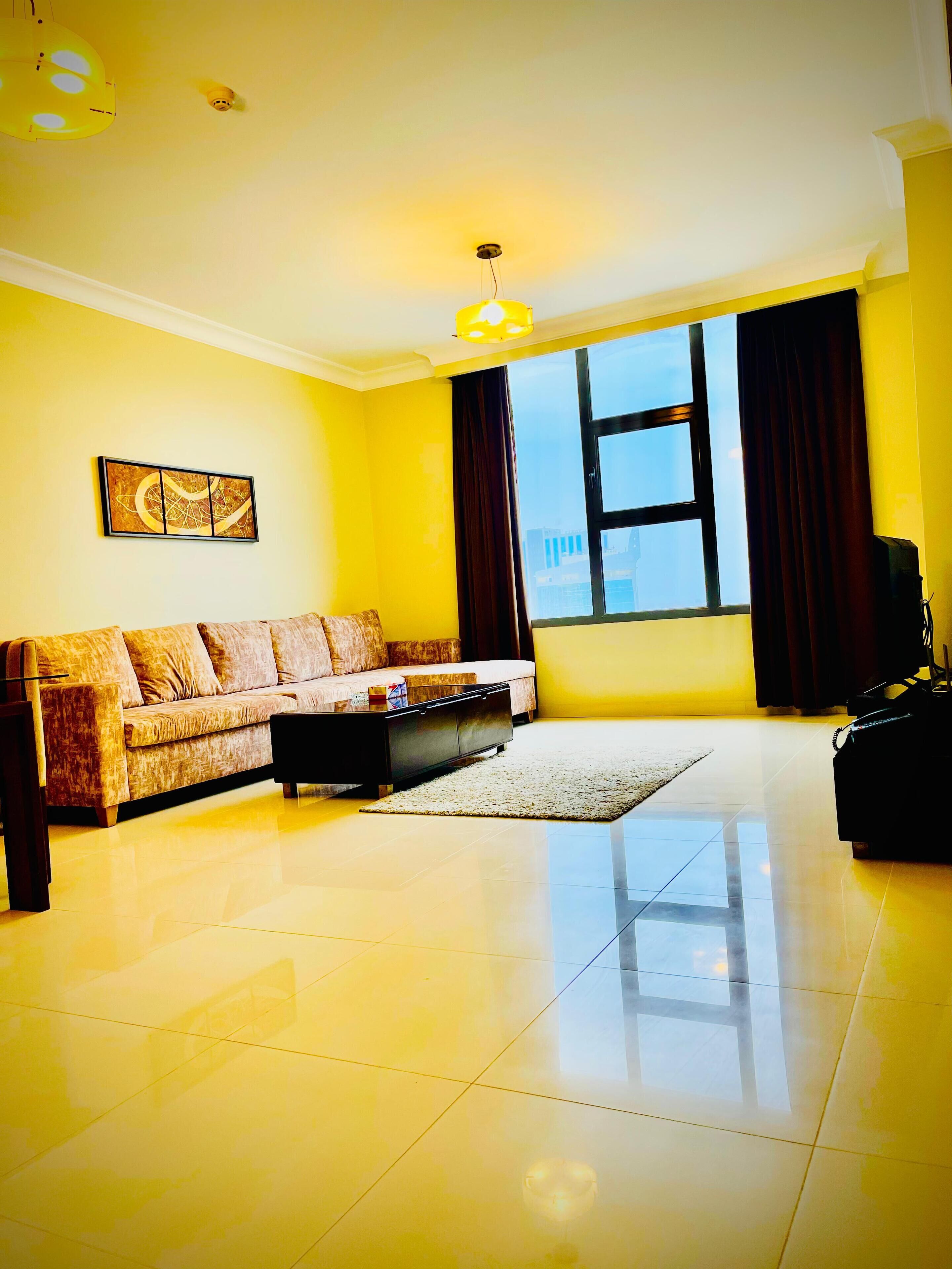 A living room with a sofa, a coffee table, a rug, a painting on the wall, and a window with curtains.