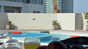 A poolside area with a pool, lounge chairs, and a table with fruit and drinks. - HAVEN TOWER (Manama)