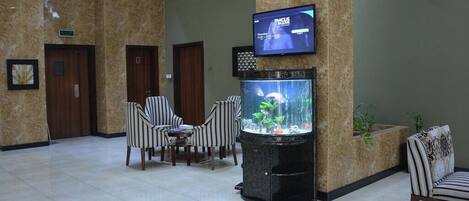 En entréhall med ett akvarium, en sittgrupp och en tv som är monterad på en pelare.