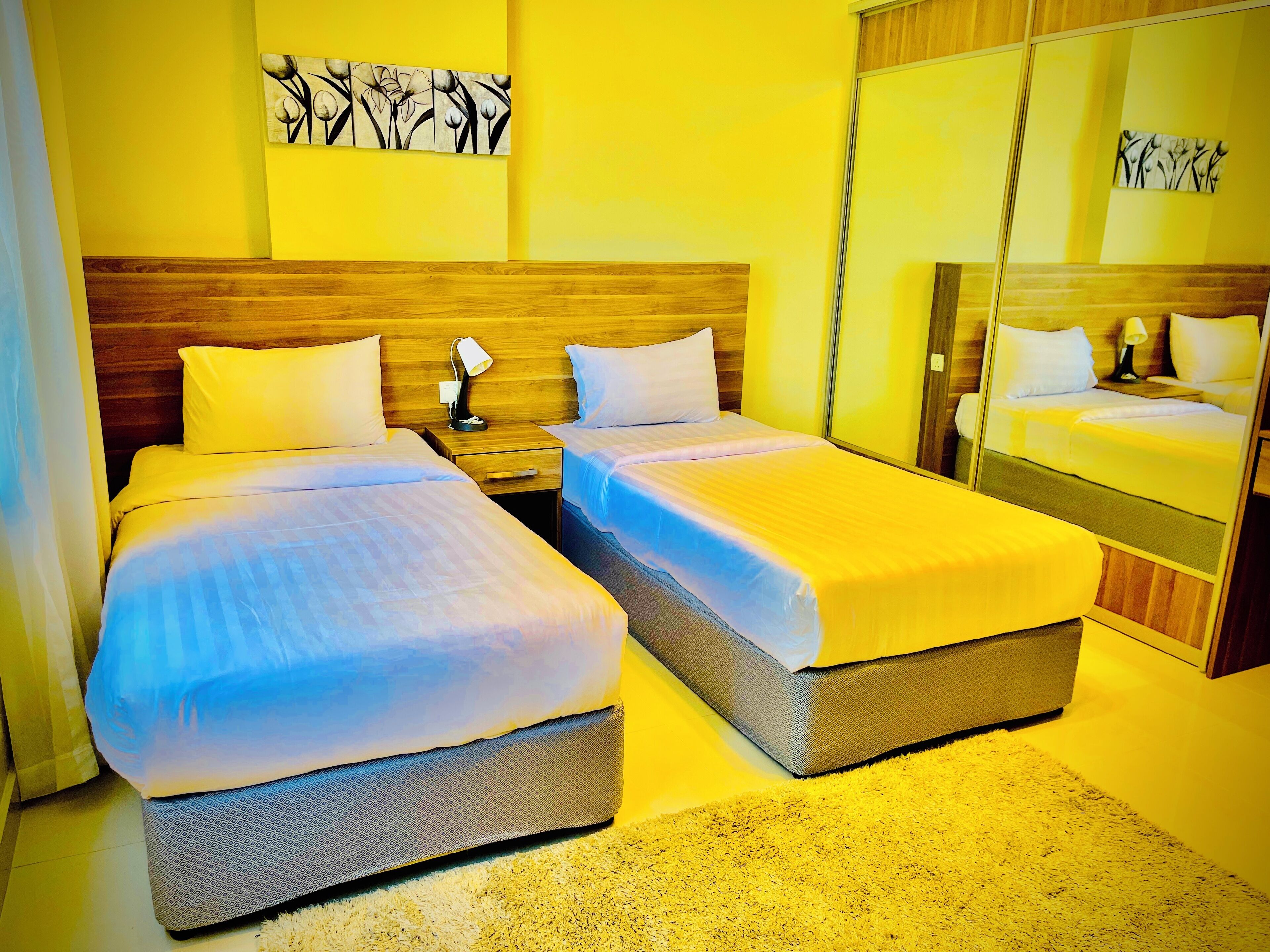 A hotel room with two beds, a wooden headboard, a nightstand with a lamp, and a large mirror.