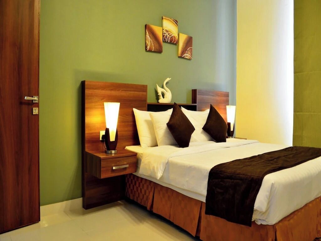 Una cama bien hecha con ropa de cama blanca y marrón, un cabecero de madera y una mesita de noche con una lámpara.